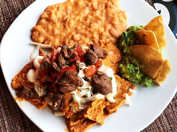 Chilaquiles rojos con arrachera, pico de gallo, crema, frijoles y guacamole con totopos.