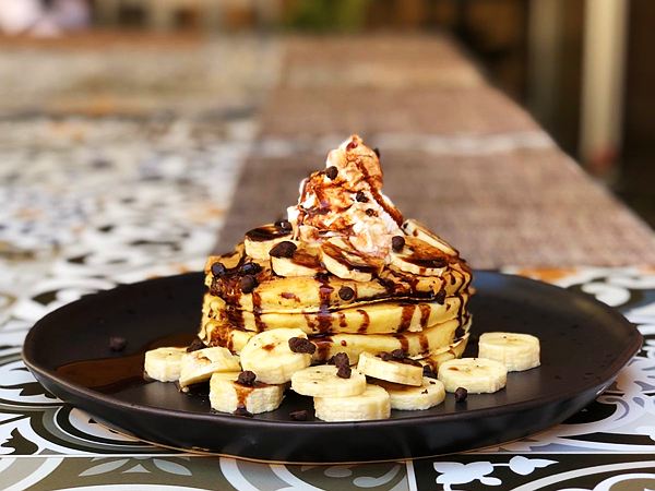 Torre de pankekes con plátano, chispas de chocolate, jarabe de chocolate y crema batida.