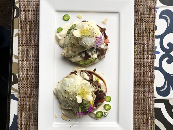 Dos sopes estilo benedicto con huevo, salsa holandesa, carne, aguacate, germinado y flores comestibles.