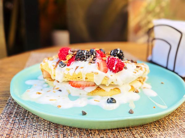 Pankeke grande doblado, relleno de yogurt, con frambuesas, zarzamoras, fresas y cereal.